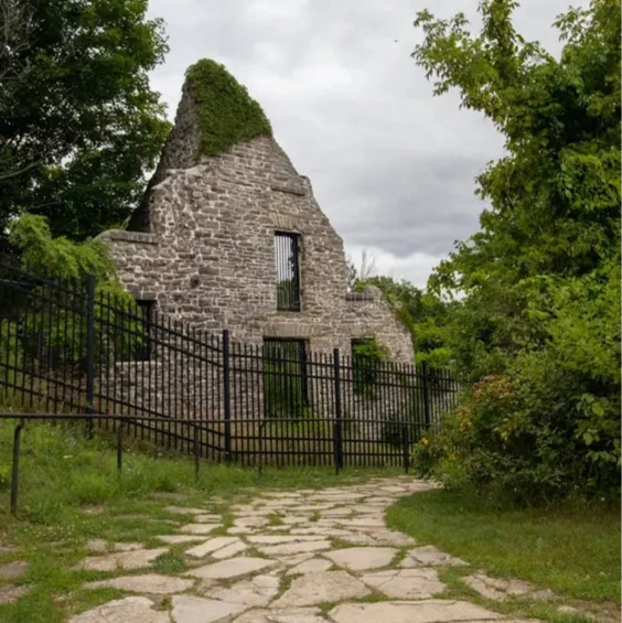 Ruins of a stone building surrounded by greenery on a cloudy day